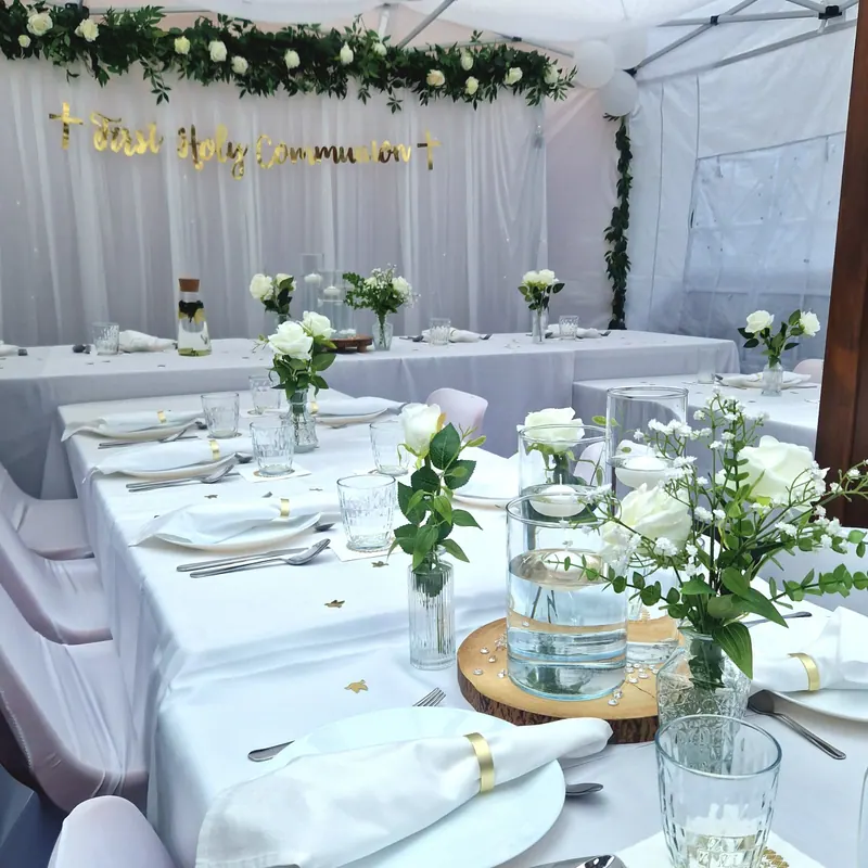 Stoły komunijne z białymi kwiatami w szklanych wazonach i girlandą z zieleni