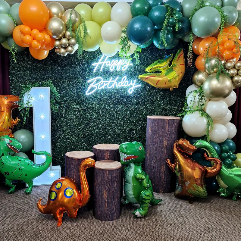 Dekoracja na pierwsze urodziny z dinozaurami, zieloną ścianką i girlandą balonową