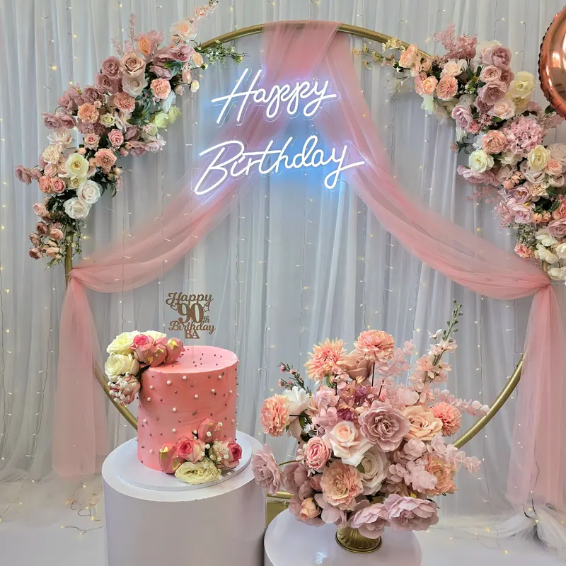 Łuk z różowymi kwiatami, draperią i neonem „Happy Birthday” oraz tort urodzinowy