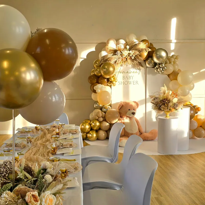 Sala na baby shower w beżu i złocie z girlandą balonową i stołami