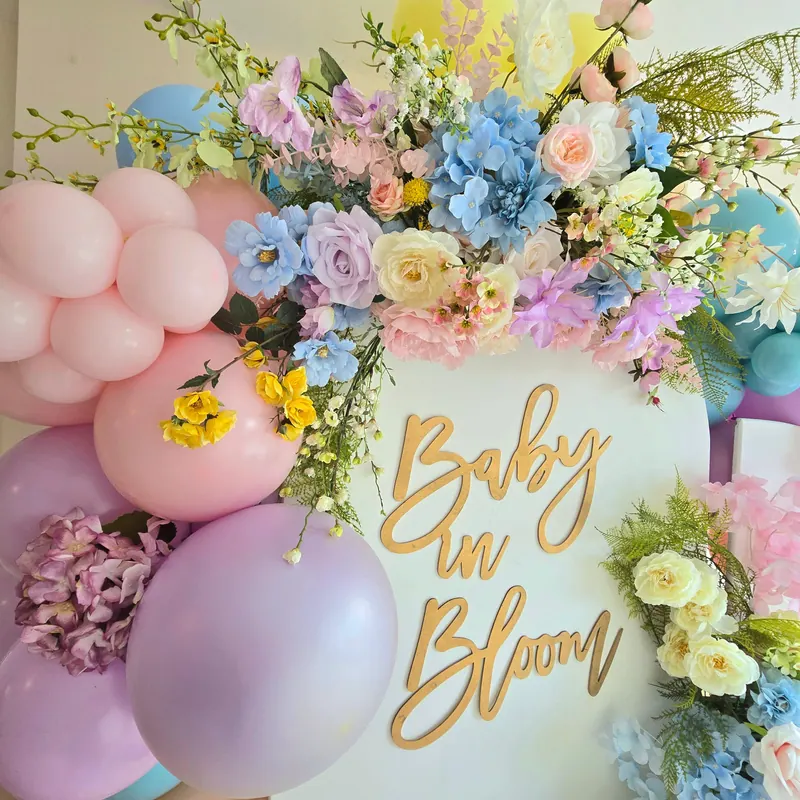 Napis „Baby in Bloom” wśród pastelowych kwiatów i balonów