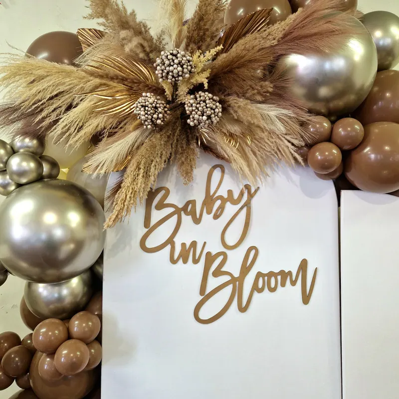 Napis „Baby in Bloom”, trawy pampasowe i balony w brązach i złocie