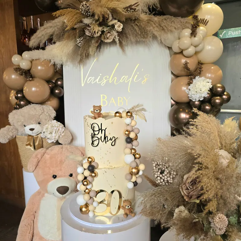 Dekoracja na baby shower z tortem, misiem, trawami pampasowymi i balonami